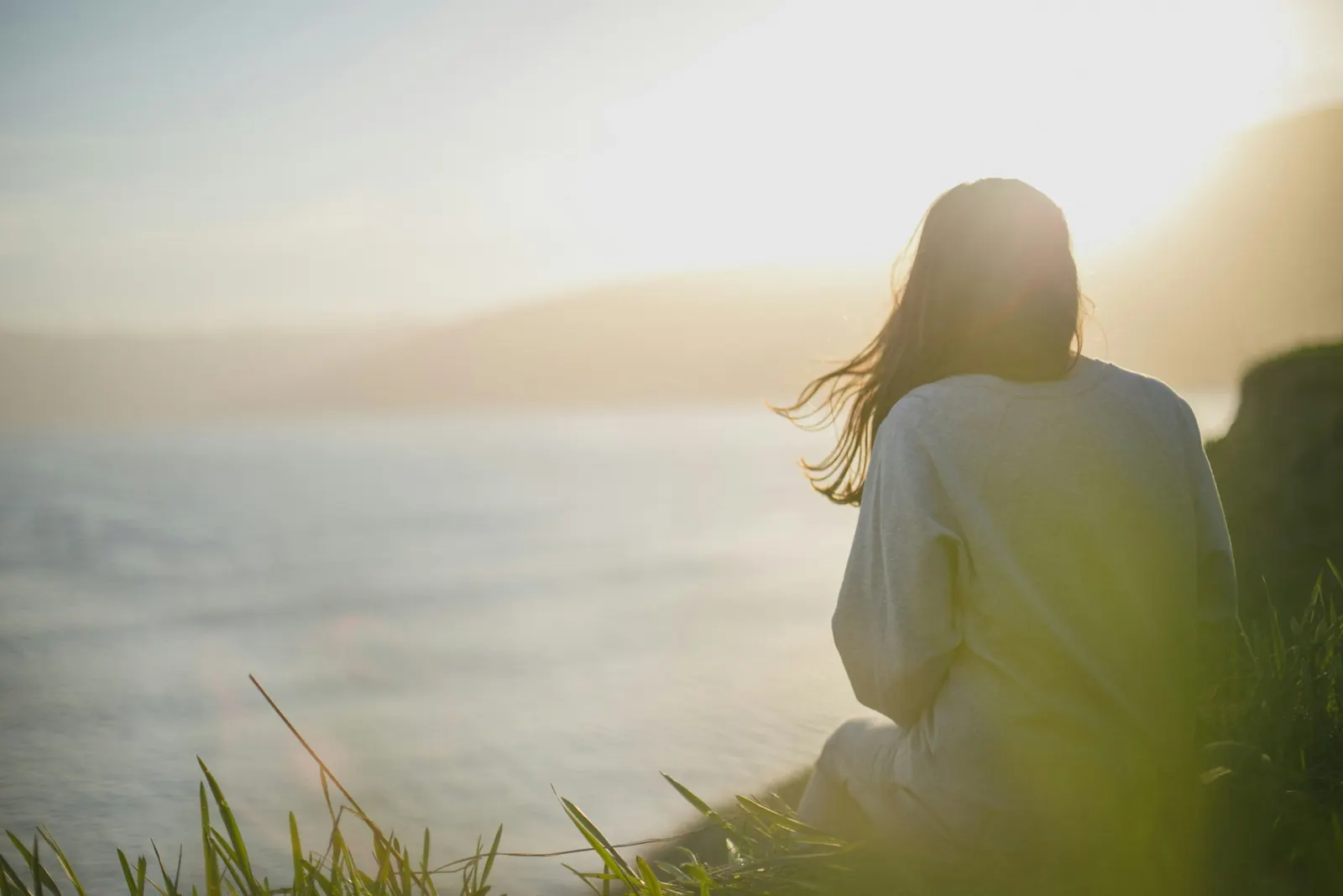 Een vrouw zit rustig aan zee en kijkt uit over het water in zacht ochtendlicht